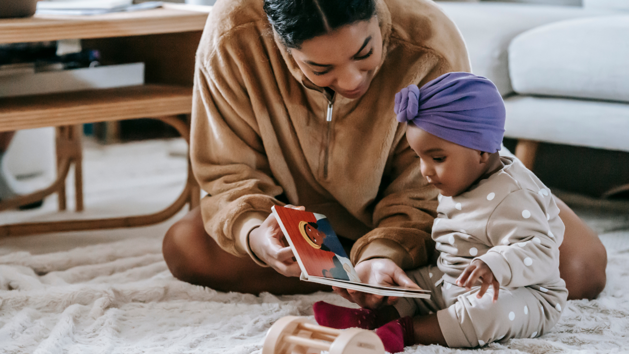 Parent and baby sitting on floor and reading a book together.